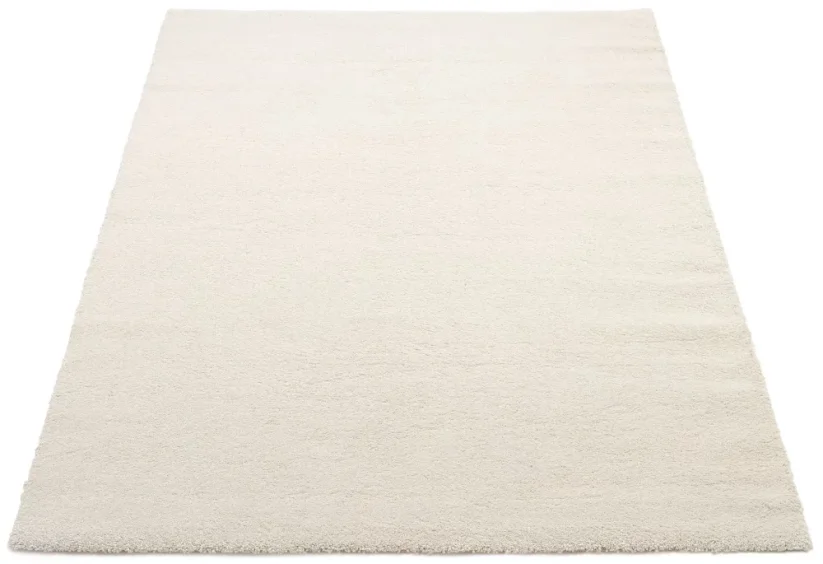 Štvorcový krémovo biely koberec je z jednej strany o niečo svetlejší ako z druhej. Je to spôsobené jemným leskom vlasu.