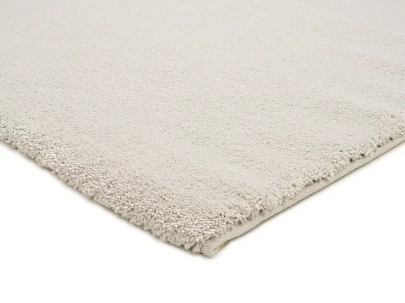 Krémovo biely štvorcový koberec má dve strany nenápadne ukončené prehnutím. Dve strany má elegantné obšitie v bielej farbe.