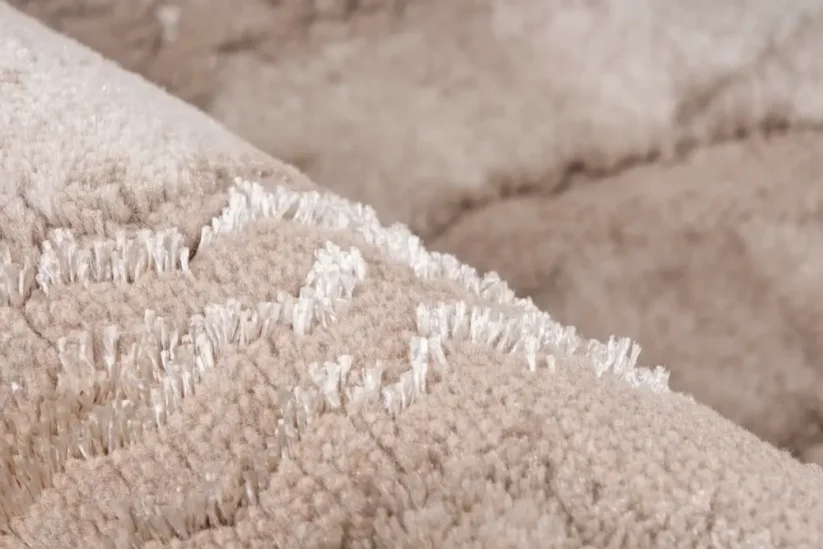 Základ koberca k posteli je béžový, mramorový dizajn je tkaný z ligotavého vlákna.